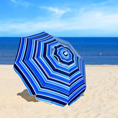 Blue striped beach umbrella on sand by the sea under a clear sky.