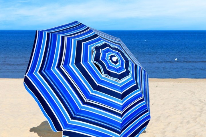 Blue striped beach umbrella on sand by the sea under a clear sky.