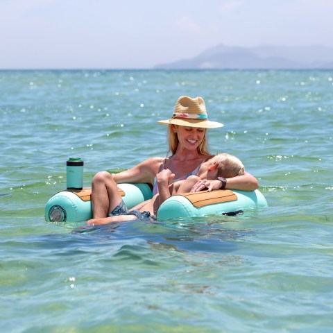 Woman in a hat relaxing on a float with a dog in clear ocean water.