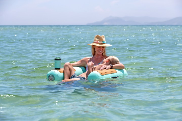 Woman in a hat relaxing on a float with a dog in clear ocean water.