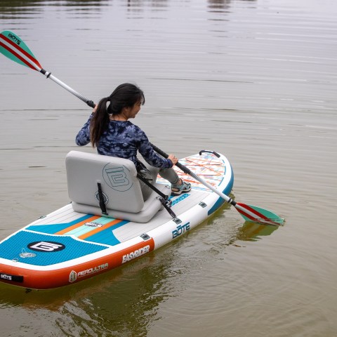 Person paddling on a lake with an inflatable paddle board.