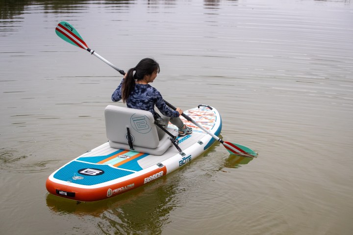 Person paddling on a lake with an inflatable paddle board.