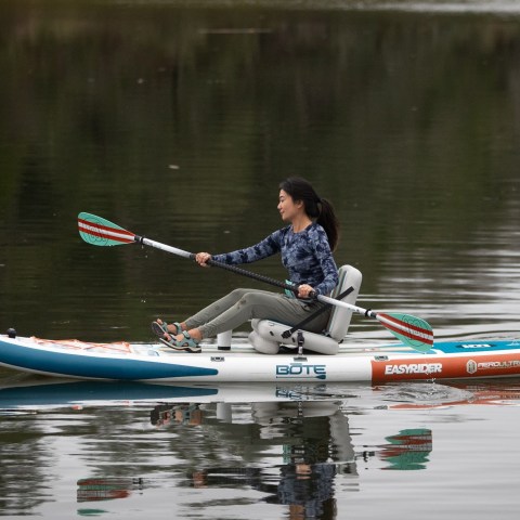 Person kayaking on calm water with a paddle board and seat.