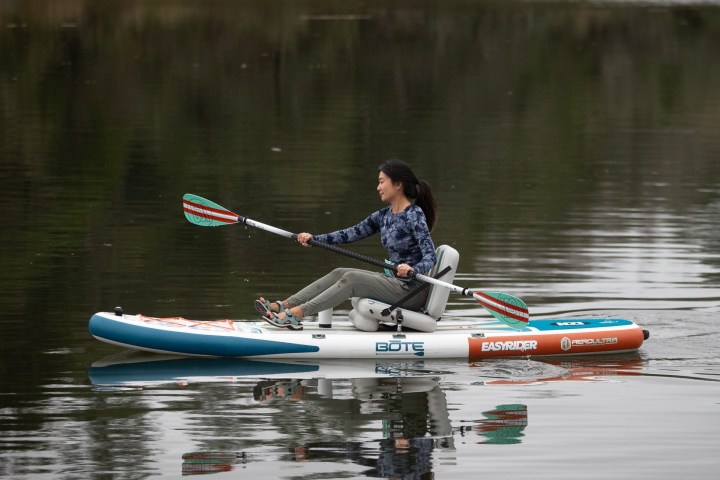 Person kayaking on calm water with a paddle board and seat.