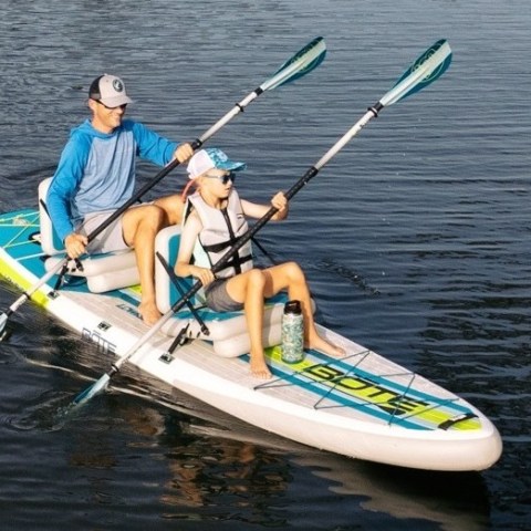 Two people in hats kayak on a paddleboard in calm water.