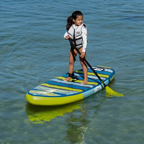Child paddleboarding on a calm lake in a life vest on a sunny day.