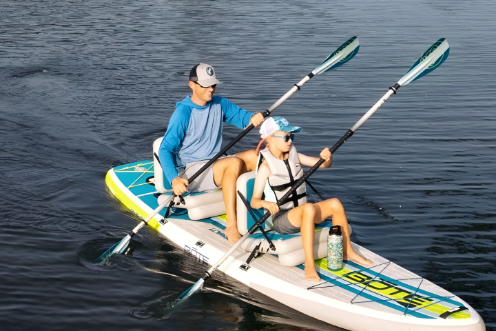 Two people kayaking on calm water, wearing hats and life jackets.