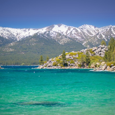 Kayakers on turquoise lake with rocky shore and snow-capped mountains in the background.