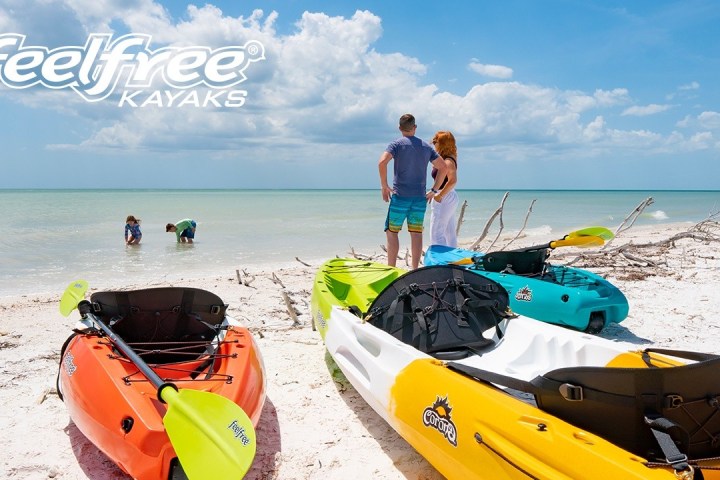 Three kayaks on a sandy beach with people by the sea under a cloudy sky.